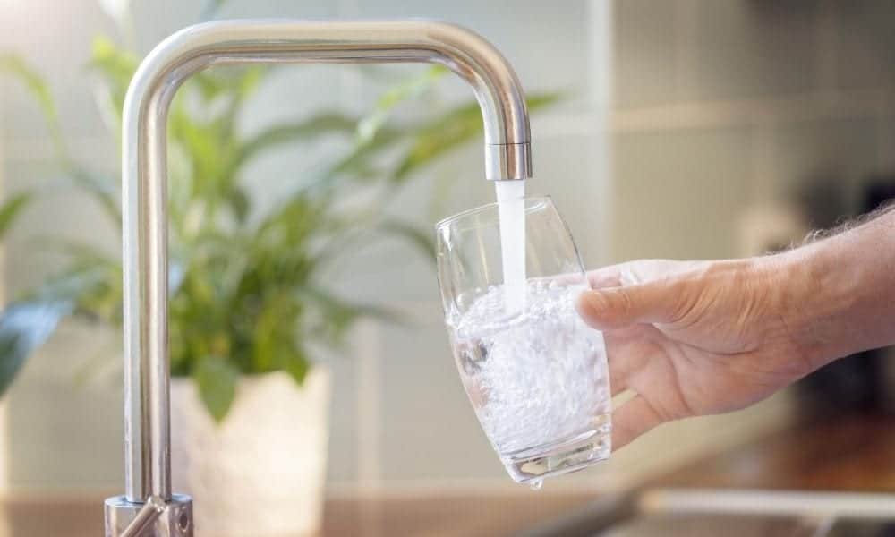 hand filling clear glass of water under a modern sink faucet