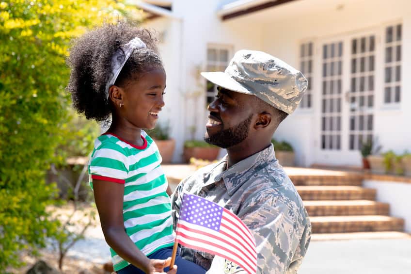 military father in uniform holding daughter who is holding an American flag