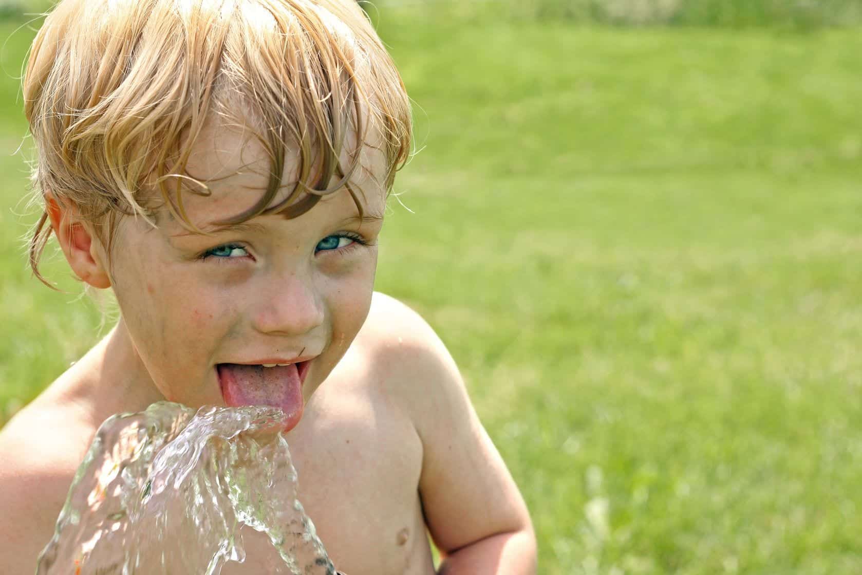 Boy drinking water from a hose shirtless dirty boy drinking water from a hose in grassy yard