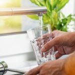 hands filling a clear glass with tap water from modern kitchen faucet