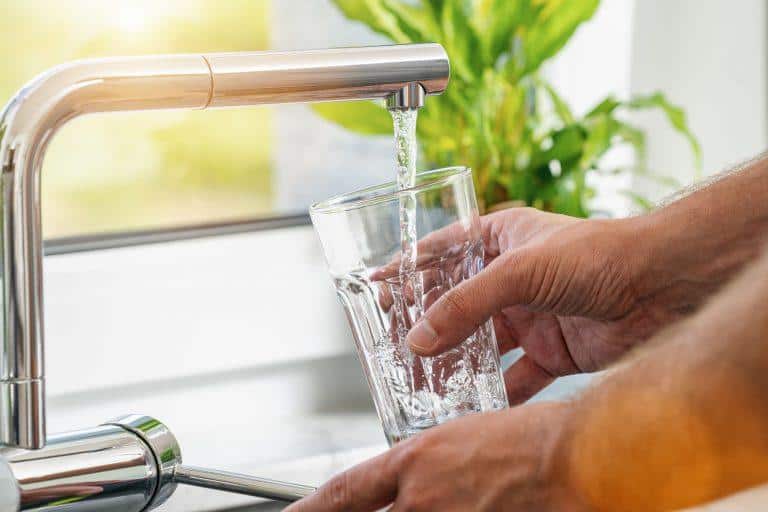 hands filling a clear glass with tap water from modern kitchen faucet