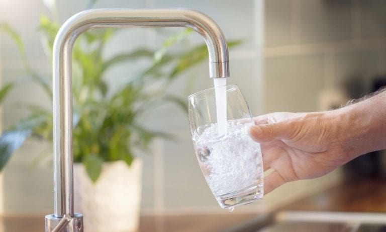 hand filling clear glass of water under a modern sink faucet