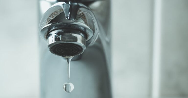 A leaky faucet with clear water droplets dripping from the spout, emphasizing the importance of fixing plumbing problems.