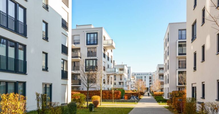 A long row of multiple large, white apartment buildings with a sidewalk running through the middle of them.