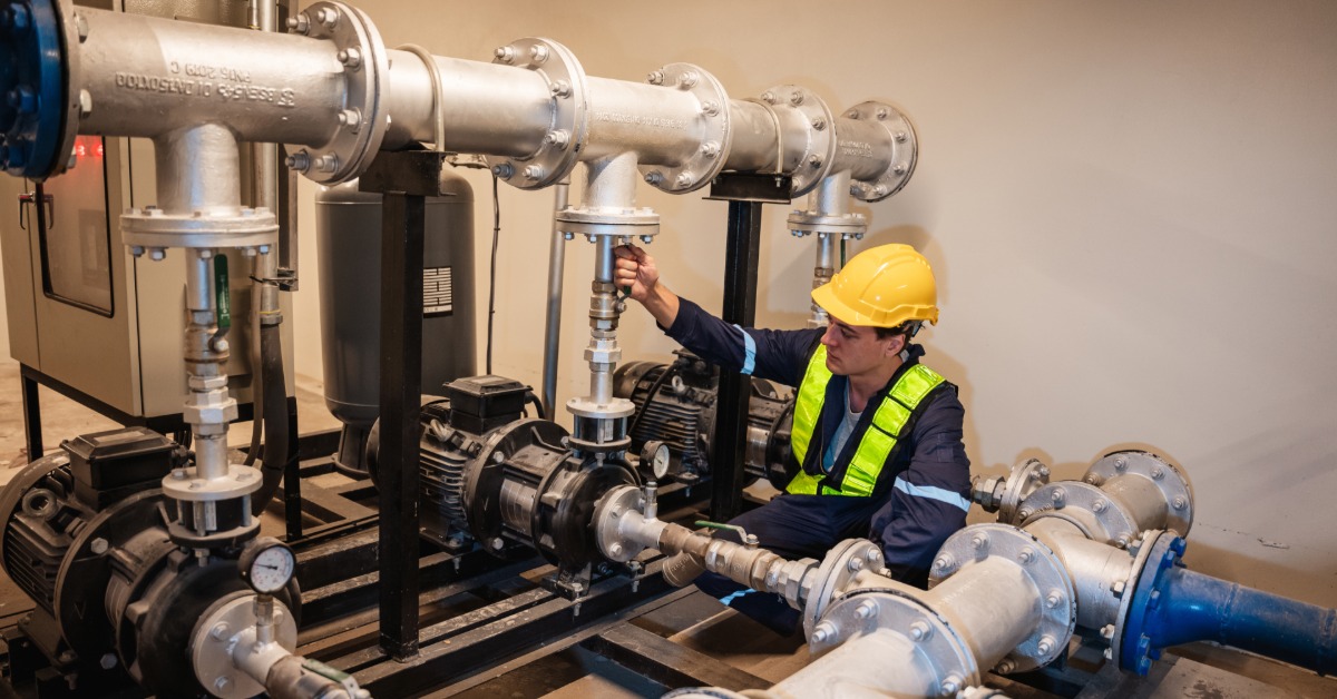An industrial worker wearing safety gear is inspecting the inside of plumbing and water valves in a large facility.