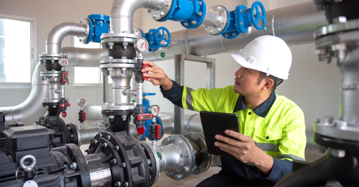 An industrial worker examining the water pressure in a water treatment station. He is wearing a hard hat and a uniform.