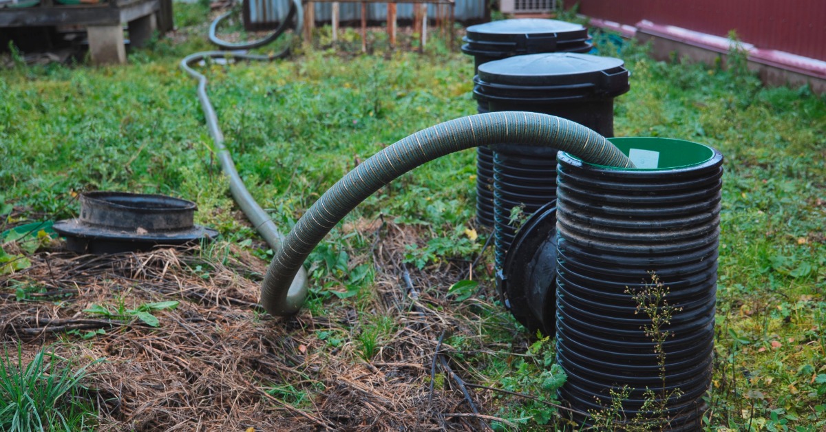 A sewage pumping service with a hose inside the septic tank that runs across the grassy rural backyard.