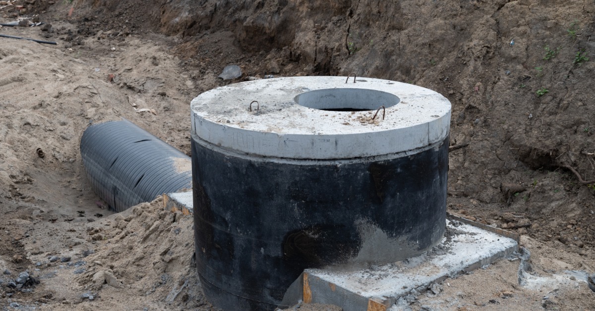 A partially constructed septic tank with unfinished piping. The site is in a residential area and surrounded by dirt.
