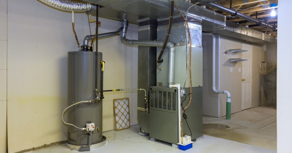 A gas water boiler tank in the basement of a house. The area around the water boiler is unfinished and bare.