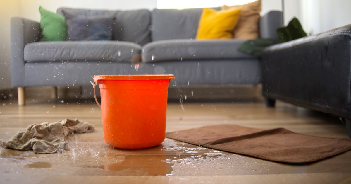 The living room of a house with an orange bucket on the floor to catch leaking water coming from the ceiling.